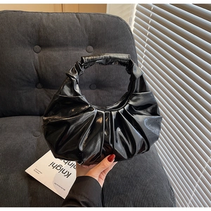 Detail of a black glossy pleated handbag with accordion folds on a textured sofa