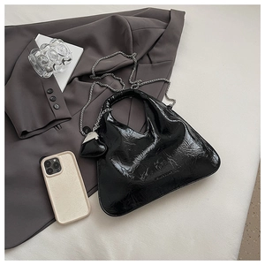 Detail of black glossy crinkled handbag with heart charm and silver chain strap