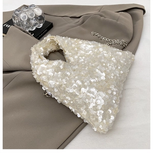 Close-up of white sequin handbag with silver chain on a beige blazer background