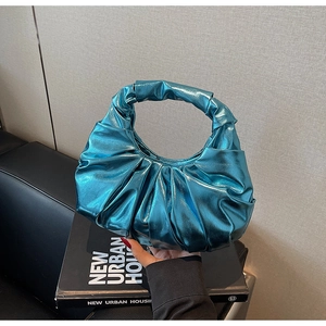 Detailed view of the metallic blue pleated evening bag on a black leather sofa