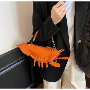 Detail of orange lobster-shaped handbag with gold studs held by a model