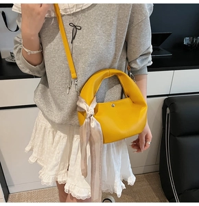 Detail of yellow grainy leather crescent bag with decorative silk scarf on handle