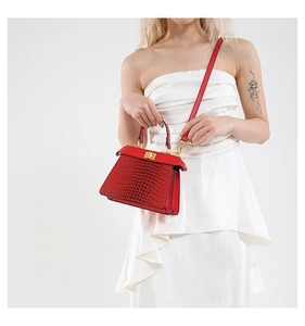 Detailed view of red crocodile pattern handbag with gold hardware on white dress
