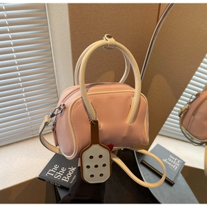 Pink bowling bag with white handles and detachable strap shown on a decorative mirror base