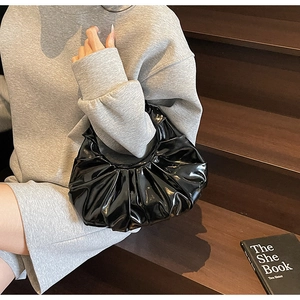 Close-up of black ruched cloud handbag featuring glossy finish and elegant pleated design