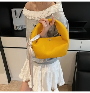 Detail of a bright yellow pebbled leather dumpling bag with decorative floral silk scarf handle