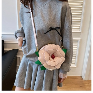 Pink camellia flower crossbody bag with pearl accents worn by a model in a luxury setting