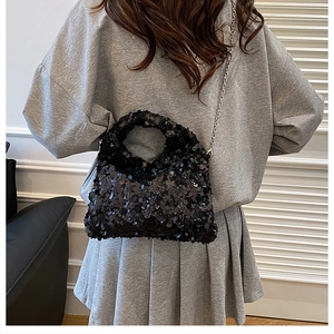 Detail of a black sequined crossbody bag with silver chain strap worn by a model