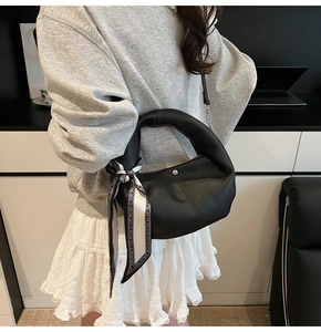 Détail du sac à main en cuir grainé noir avec foulard en soie et boucle métallique