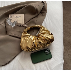 Top view of a gold pleated metallic hobo bag on a brown blazer with elegant lifestyle accessories