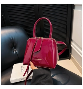 Detail of glossy shell-shaped handbag in magenta with gold logo and dual zippers