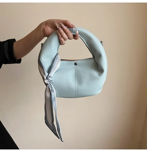 Close-up of light blue lychee leather handbag with elegant printed silk scarf handle
