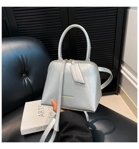 Detail of glossy shell bag in light blue with gold lettering and slim shoulder strap