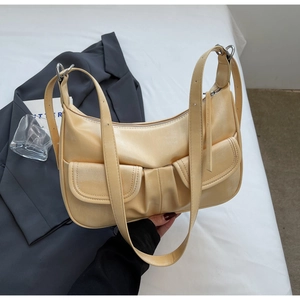 Detail view of beige crescent bag featuring dual front pockets and glossy satin finish