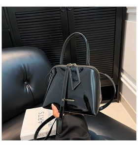 Close-up of glossy black shell bag featuring golden logo and polished patent leather texture