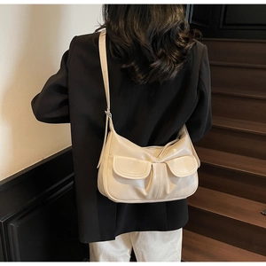 Detail view of a beige dumpling-shaped shoulder bag with front flap pockets on a model