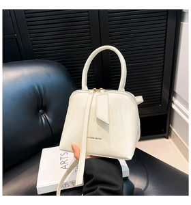 Detail of a creamy white shell-shaped glossy handbag showing a top handle and logo print