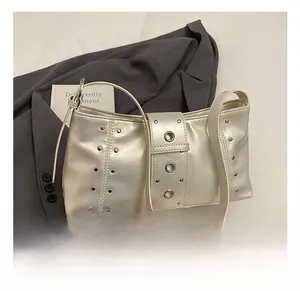 Detail of cream baguette bag with silver rivets and eyelet strap on grey suit