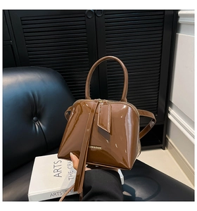 Detailed macro view of dark brown glossy patent leather shell bag with gold fashion lettering
