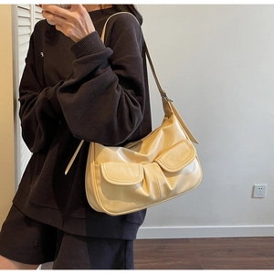 Minimalist cream hobo bag shown on shoulder with stylish pleated front flap pockets