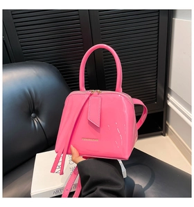 Macro detail of glossy fluorescent pink shell bag featuring gold fashion logo and long tassels