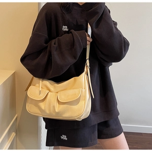 Detail view of cream crossbody bag featuring two front pleated pockets and adjustable strap