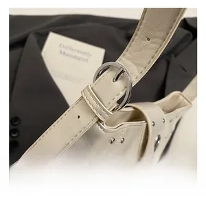 Detail of adjustable strap with silver buckle and rivets on cream faux leather tote bag