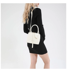 Close-up of cream glossy shell bag with metal handles shown on a model in black dress