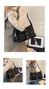 Detail of black patent leather underarm bag featuring silver rivets and metal eyelet buckle