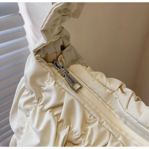 Close-up of the smooth silver zipper and quilted ruched fabric of the cream cloud bag