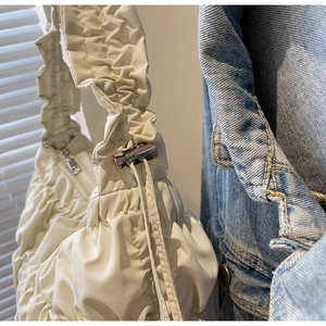 Close-up of cream pleated puff bag featuring metal drawstring buckle and nylon texture