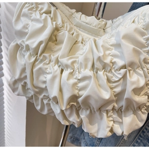 Detail of white puffer shoulder bag featuring quilted texture and silver metal zipper