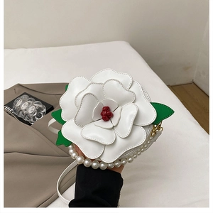 Detail of white 3D camellia shaped bag with pearl handle and green leaf accent