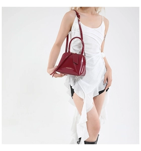 Detail of red glossy patent leather shell bag with gold hardware and shoulder strap