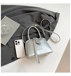 Detail of silver metallic shell bag with logo, zipper pull and elegant handle
