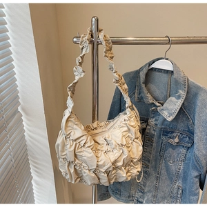 Close-up of cream pleated cloud shoulder bag with quilted details on metal display stand