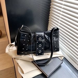 Chic black glossy shoulder bag with silver rivets and metal rings on beige coat