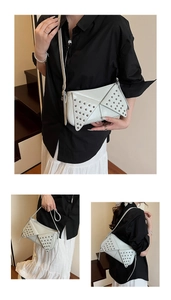 Détail du sac sous le bras crème avec rivets métalliques sur une tenue noir et blanc
