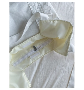 Detail of white canvas tote bag featuring lace trim, metal zipper pocket and velcro closure