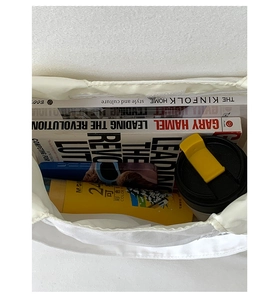 Top-down view of spacious white pleated tote bag showing daily items like books and bottles