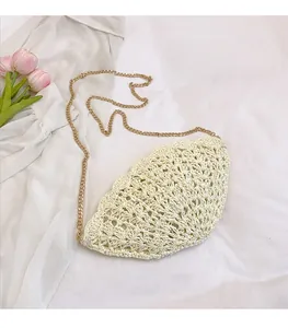 Detail of hollow-out shell shaped straw crossbody bag with golden chain strap on white fabric