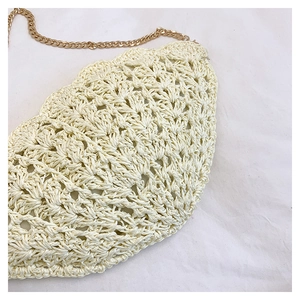 Close-up of beige woven straw handbag featuring hollow texture and gold chain strap