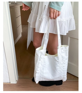 Detail of white canvas tote bag featuring delicate lace ruffles on both sides