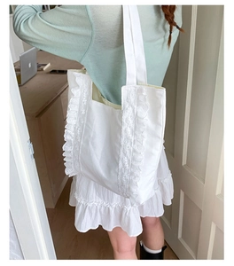 Close-up of white canvas tote bag featuring delicate lace ruffled edges and cotton straps