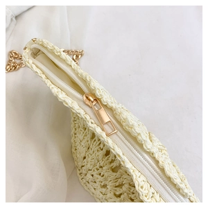Detailed close-up of beige woven straw bag featuring gold zipper and metal chain strap