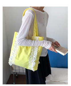 Detail of yellow canvas tote bag with white lace trim and shoulder strap on model
