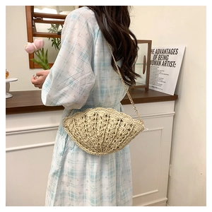 Detail of beige shell-shaped woven straw bag with golden chain strap on a model
