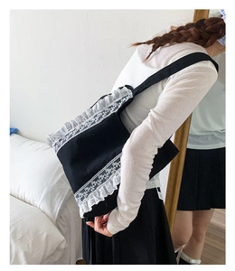 Detail of black canvas tote bag featuring white floral lace edges and ruffled trim on shoulder