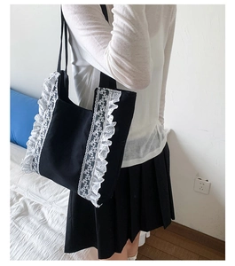Close-up of black canvas tote bag with white lace trim detail shown on shoulder