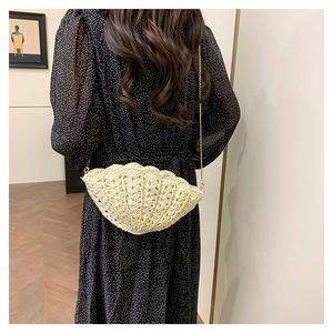 Detail of cream shell-shaped woven crossbody bag with gold chain strap on a model